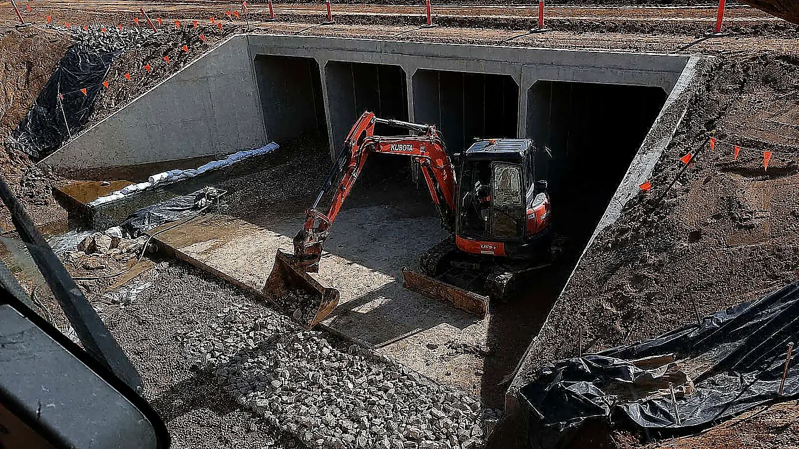 AreeCivil Constructions excavation at a concrete culvert Kubota excavator working inside a box culvert, placing rock from the cab of a second machine