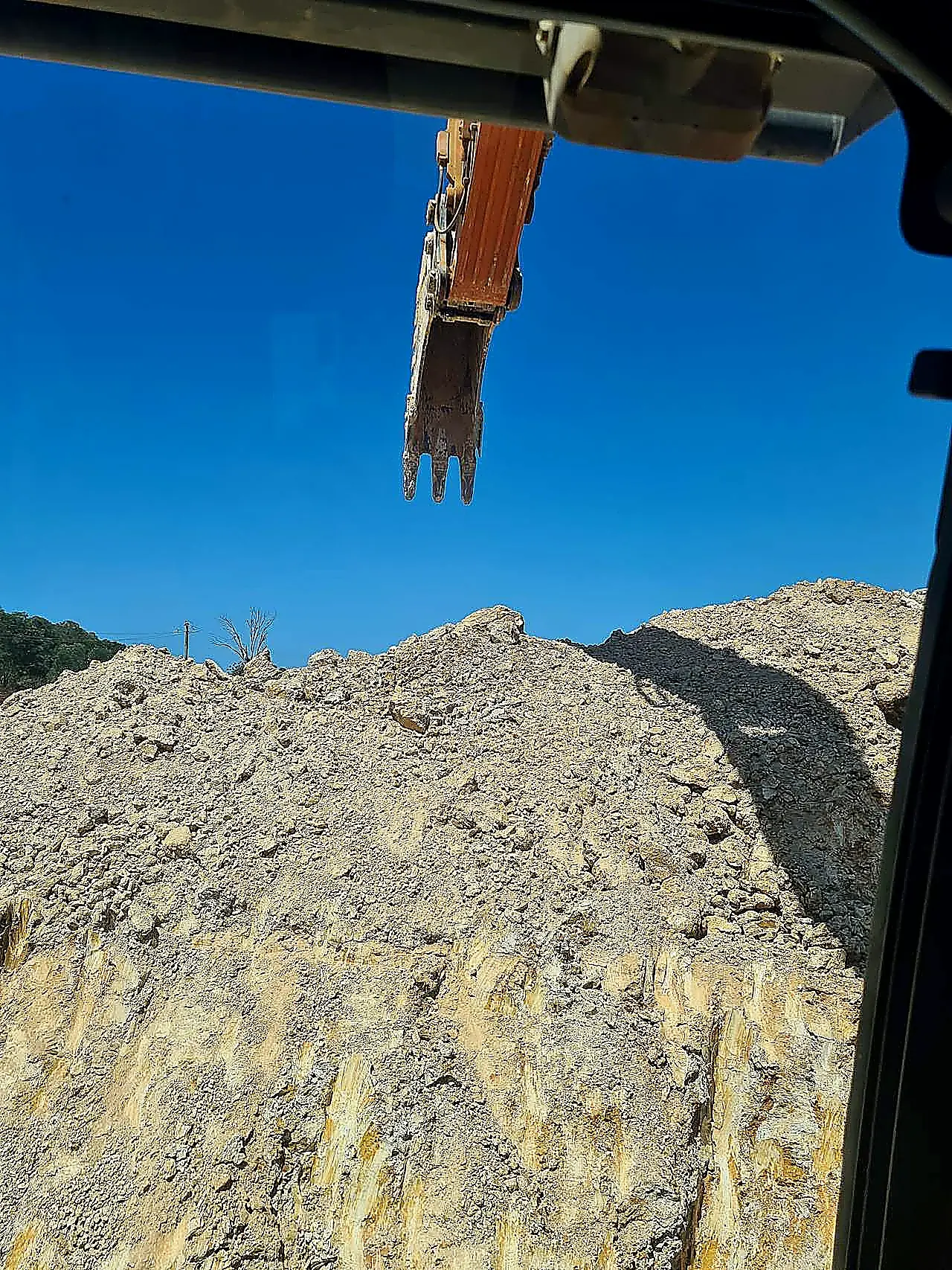 Detailed excavation — site cut and batter face, SEQ Excavator bucket above a weathered sandstone and clay cut face, photographed from the operator cab on a South East Queensland civil site.