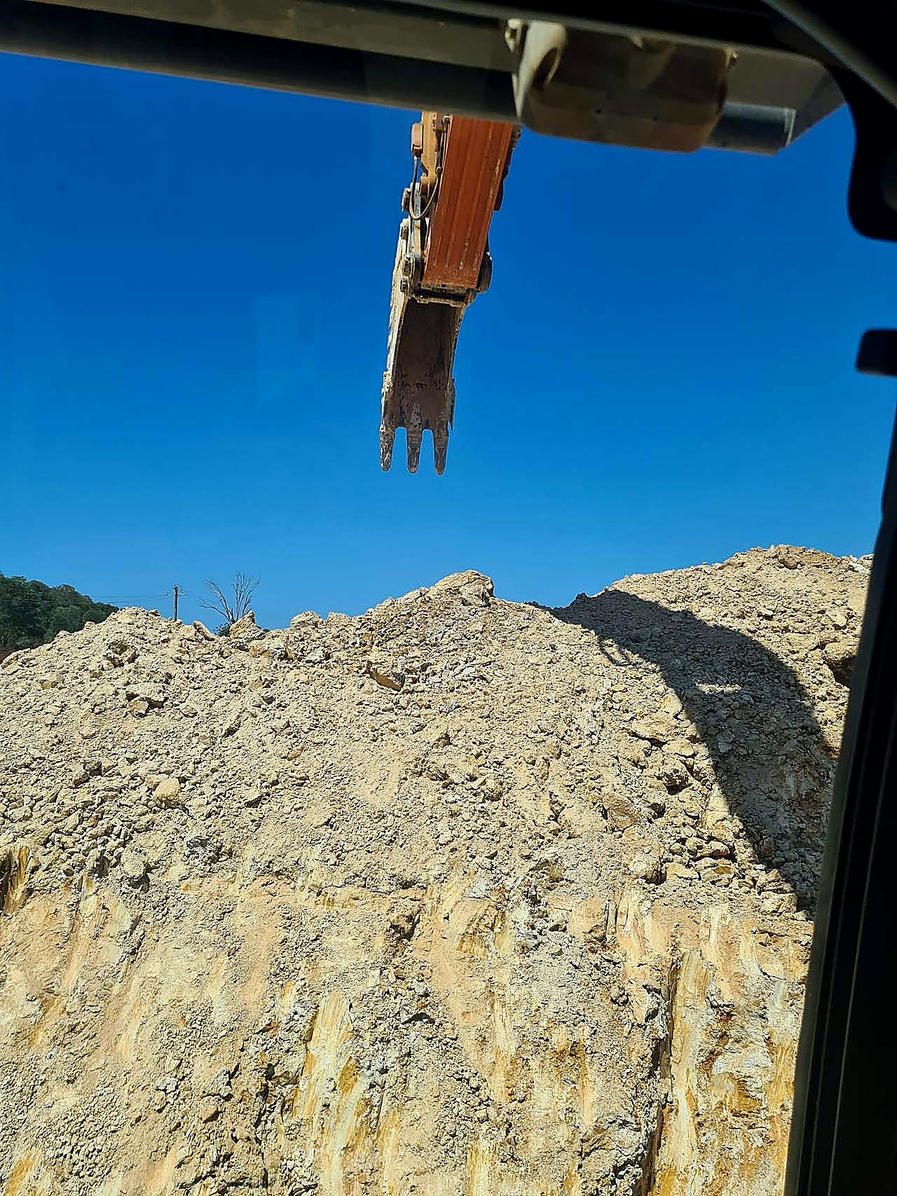 Detailed excavation — site cut and batter face, SEQ Excavator bucket above a weathered sandstone and clay cut face, photographed from the operator cab on a South East Queensland civil site.