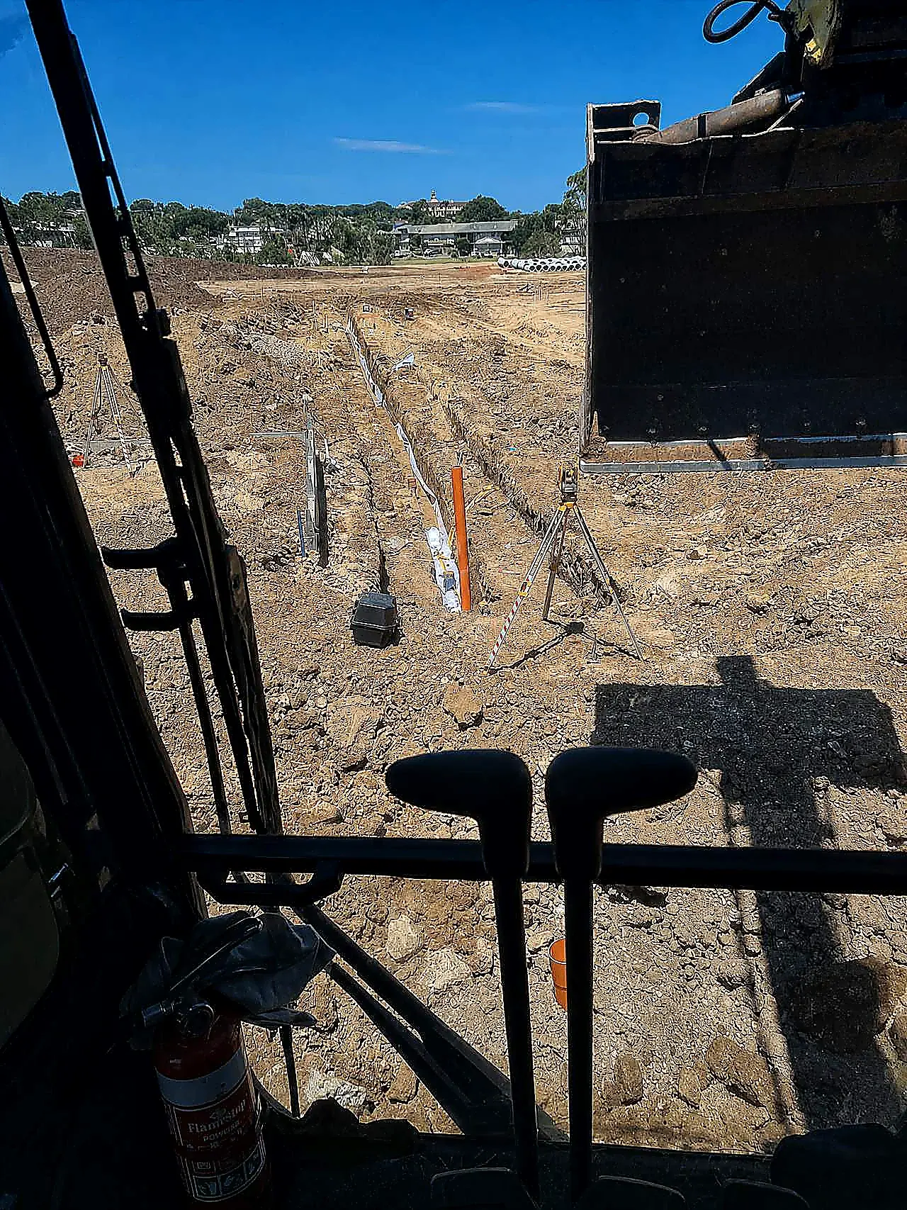 AreeCivil Constructions gravity trench from the excavator cab Open gravity trench with pipe laser and survey gear, photographed from the excavator cab on an SEQ civil site