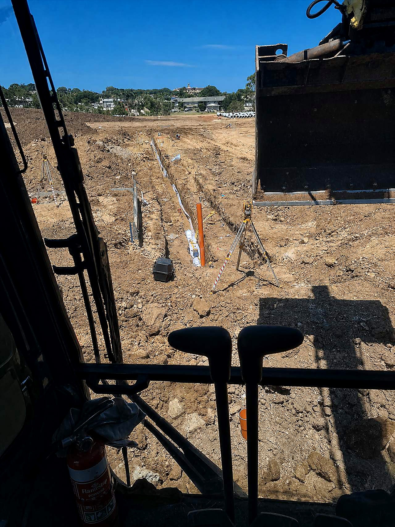 AreeCivil Constructions gravity trench from the excavator cab Open gravity trench with pipe laser and survey gear, photographed from the excavator cab on an SEQ civil site